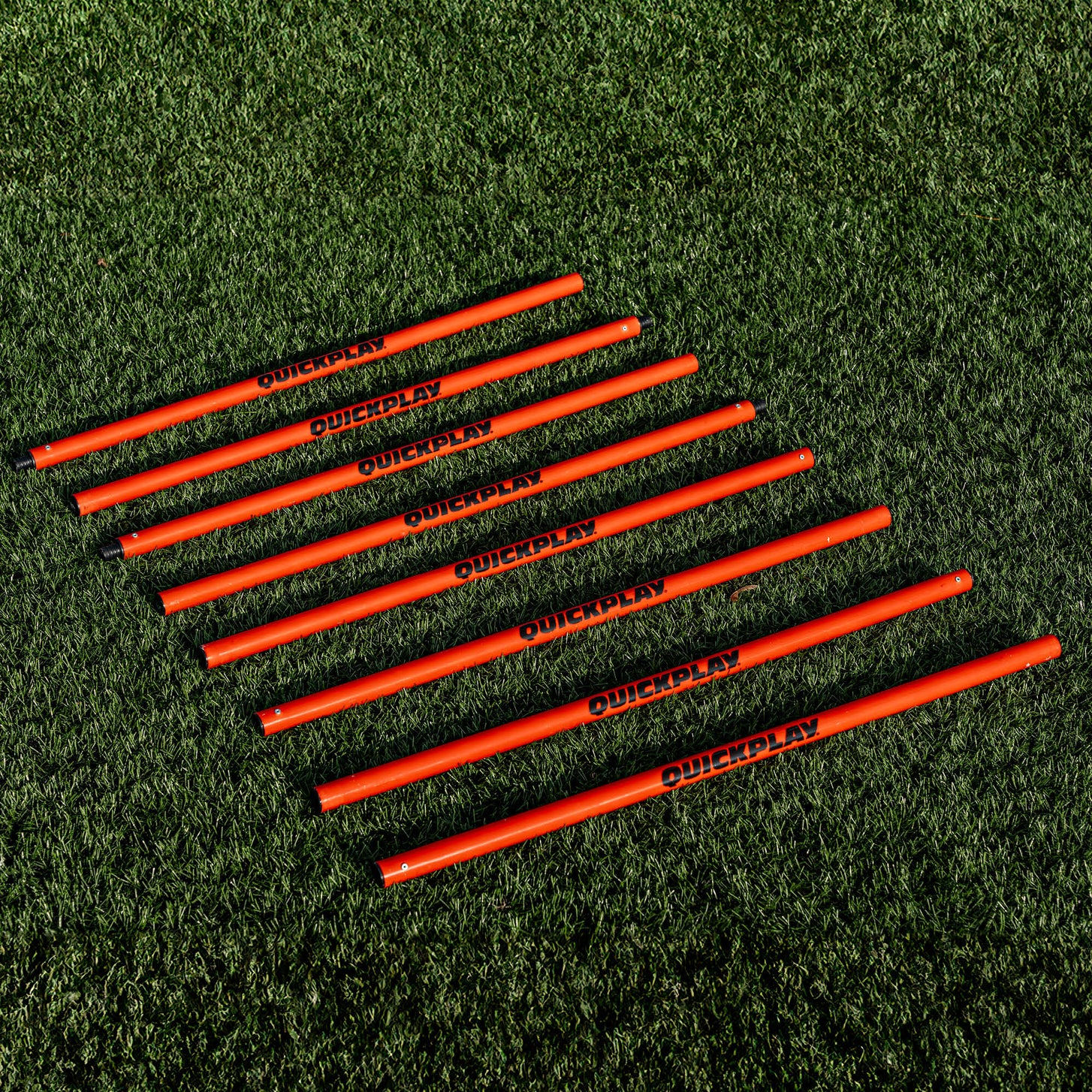 Training Poles: red QUICKPLAY pole sections laid side by side in a row on artificial turf.