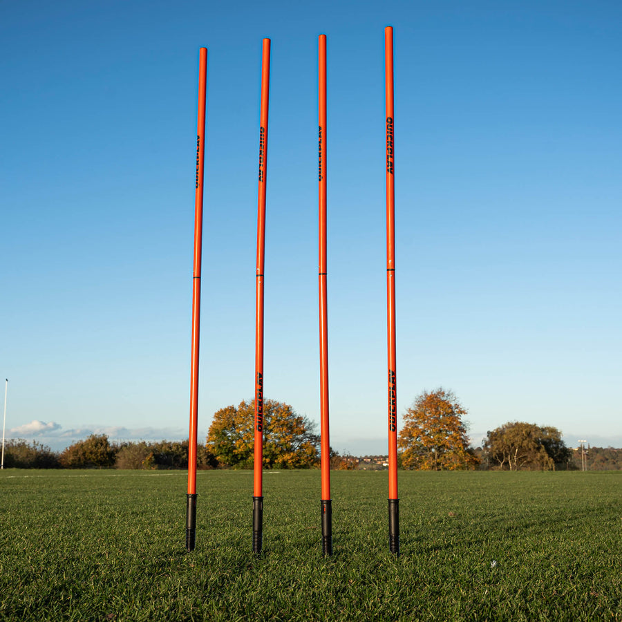A set of four red training poles with sprung stake bases on a grass field, designed for speed and agility training.