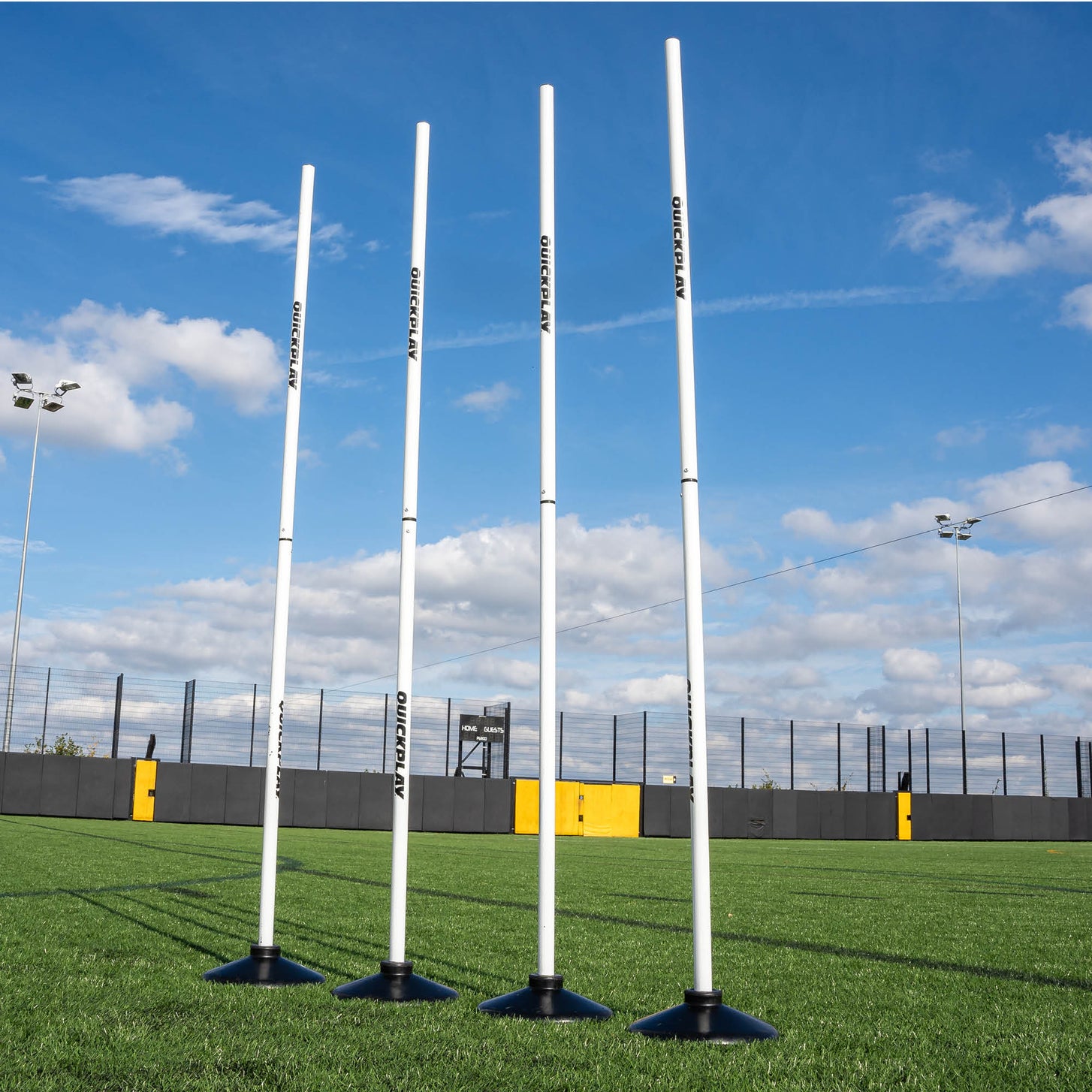A set of four white training poles with weighted bases on a grass field, designed for speed and agility training.