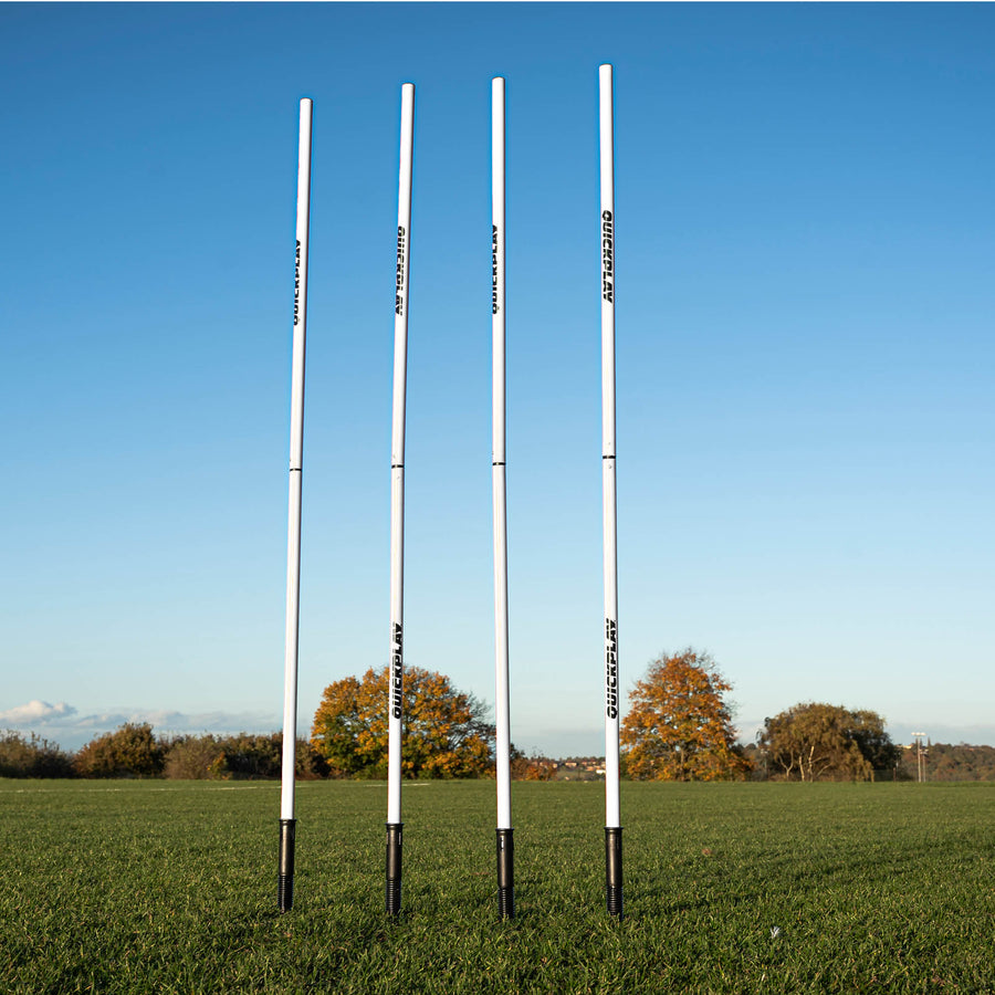 A set of four white training poles with sprung stake bases on a grass field, designed for speed and agility training.