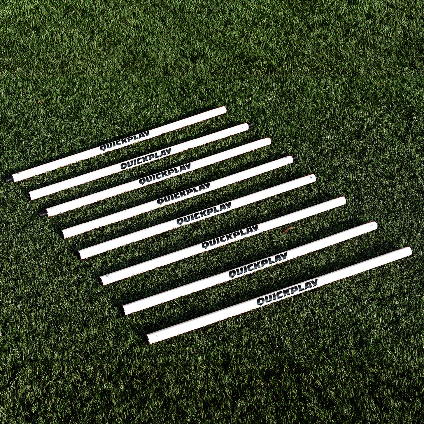 Training Poles: white QUICKPLAY pole sections laid side by side in a row on artificial turf.
