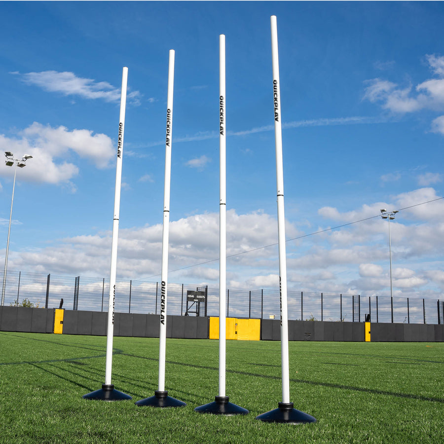 A set of four white training poles with weighted bases on a grass field, designed for speed and agility training.