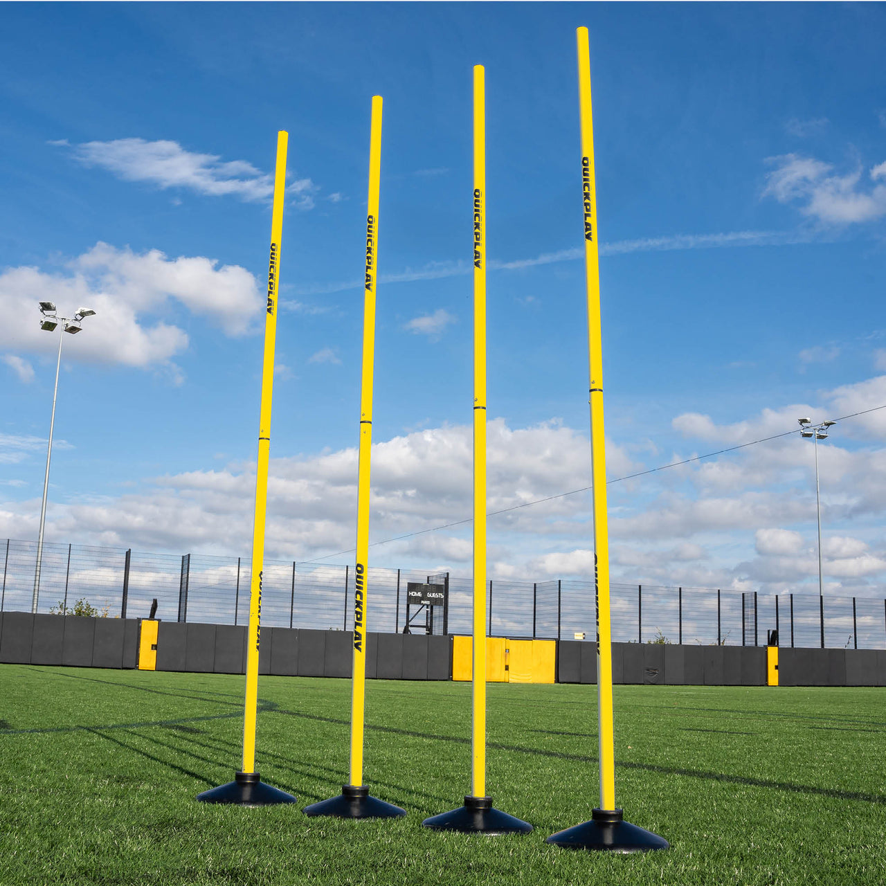 A set of four yellow training poles with weighted bases on a grass field, designed for speed and agility training.