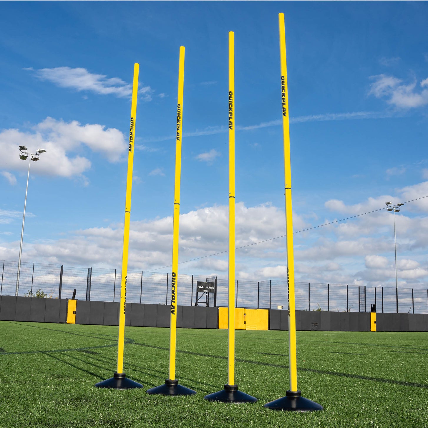 A set of four yellow training poles with weighted bases on a grass field, designed for speed and agility training.