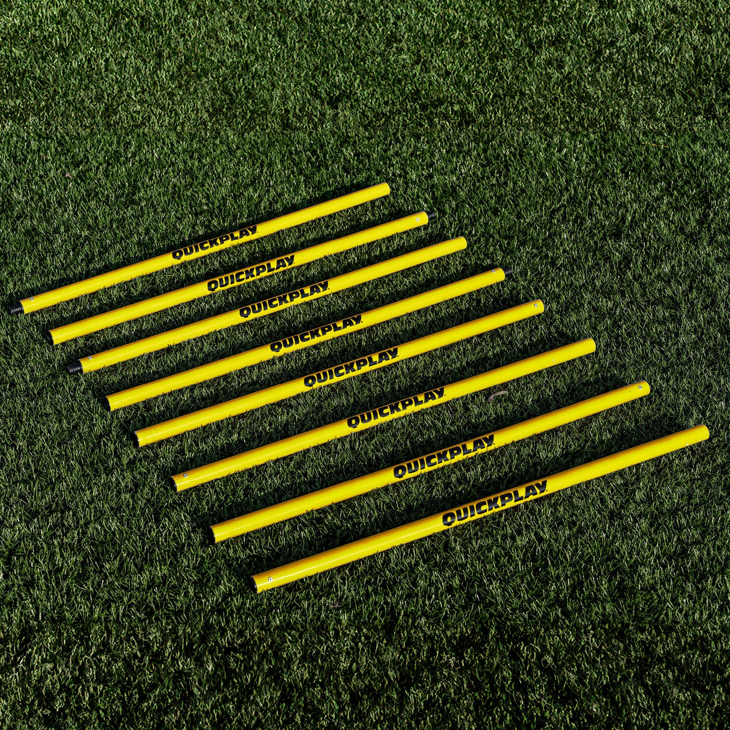 Training Poles: yellow QUICKPLAY pole sections laid side by side in a row on artificial turf.