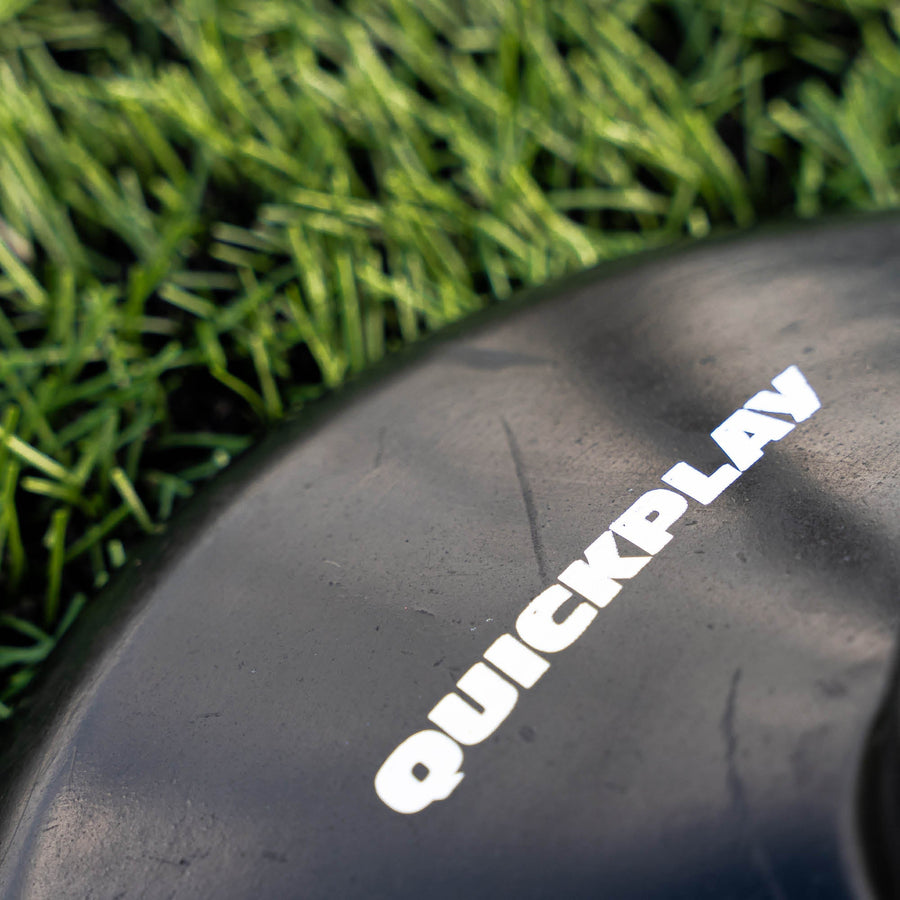Close up shot of a black training pole base with 'QuickPlay' branding on a grass field.