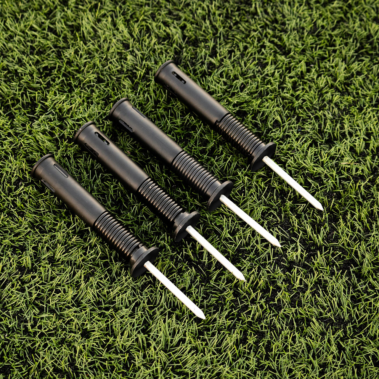 Four black sprung ground stakes on a green grass background