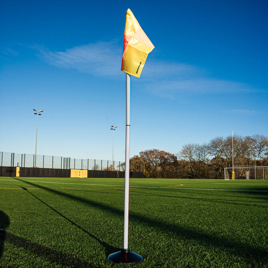 Yellow & orange corner flag on a pole in a sports field with a clear blue sky