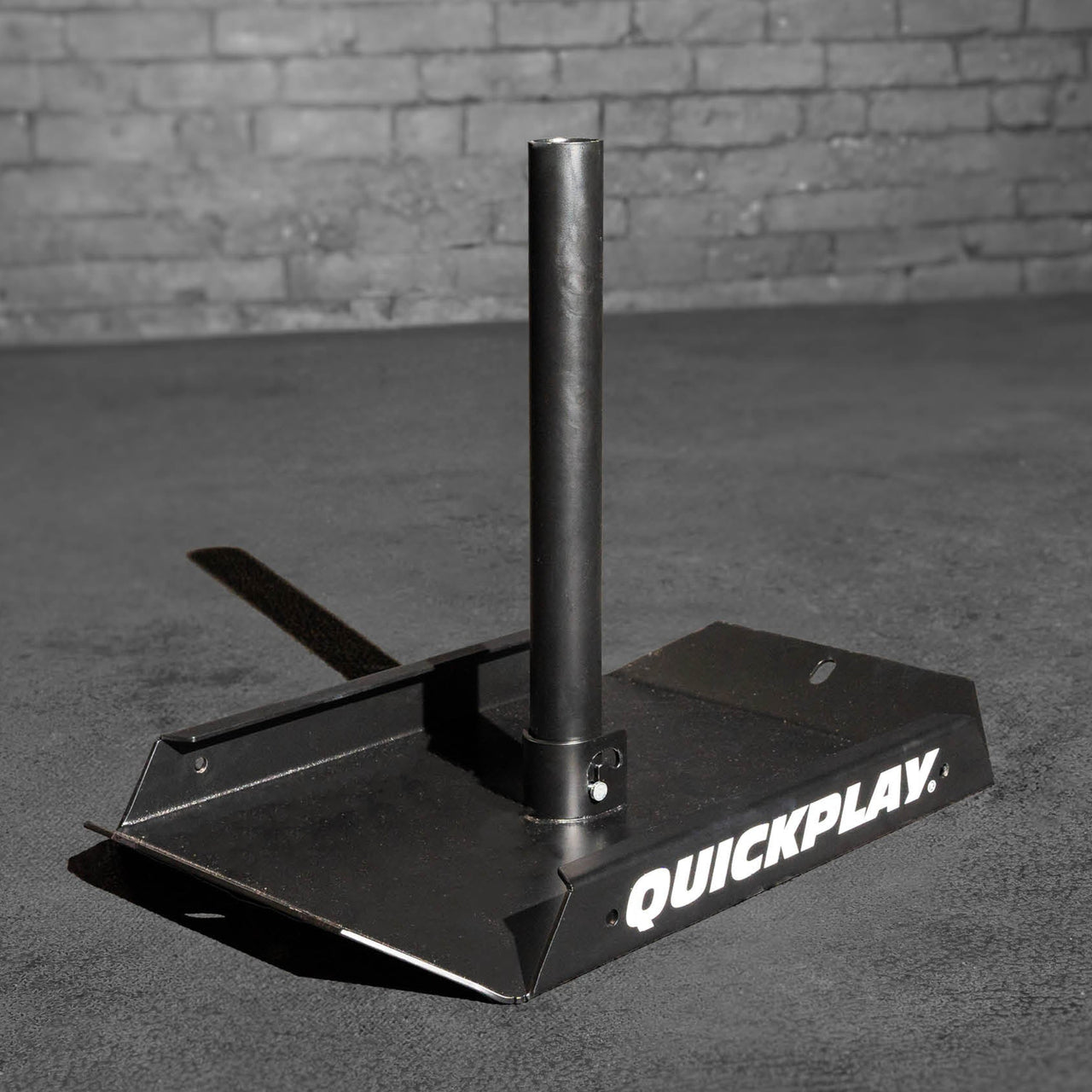 Black metal pull sled with 'Quickplay' branding on a gray surface against a brick wall.