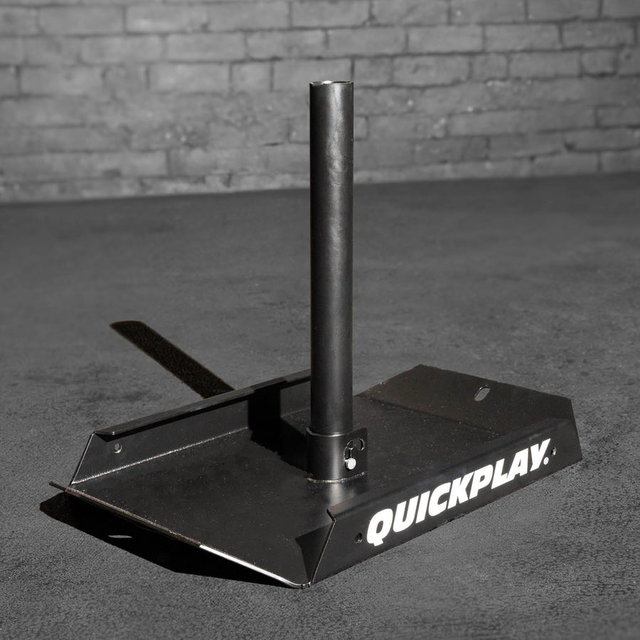 Black metal pull sled with 'Quickplay' branding on a gray surface against a brick wall.