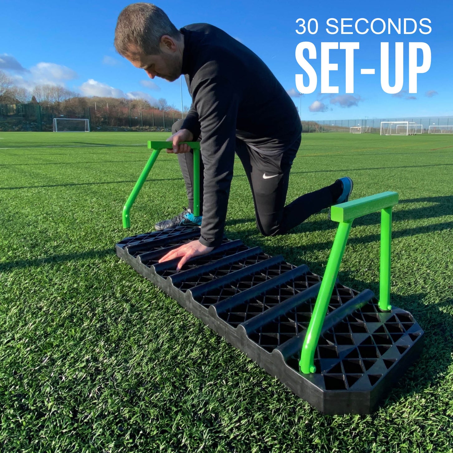 REPLAY Station XL board with a man kneeling on an artificial field to fit its green rear supports.