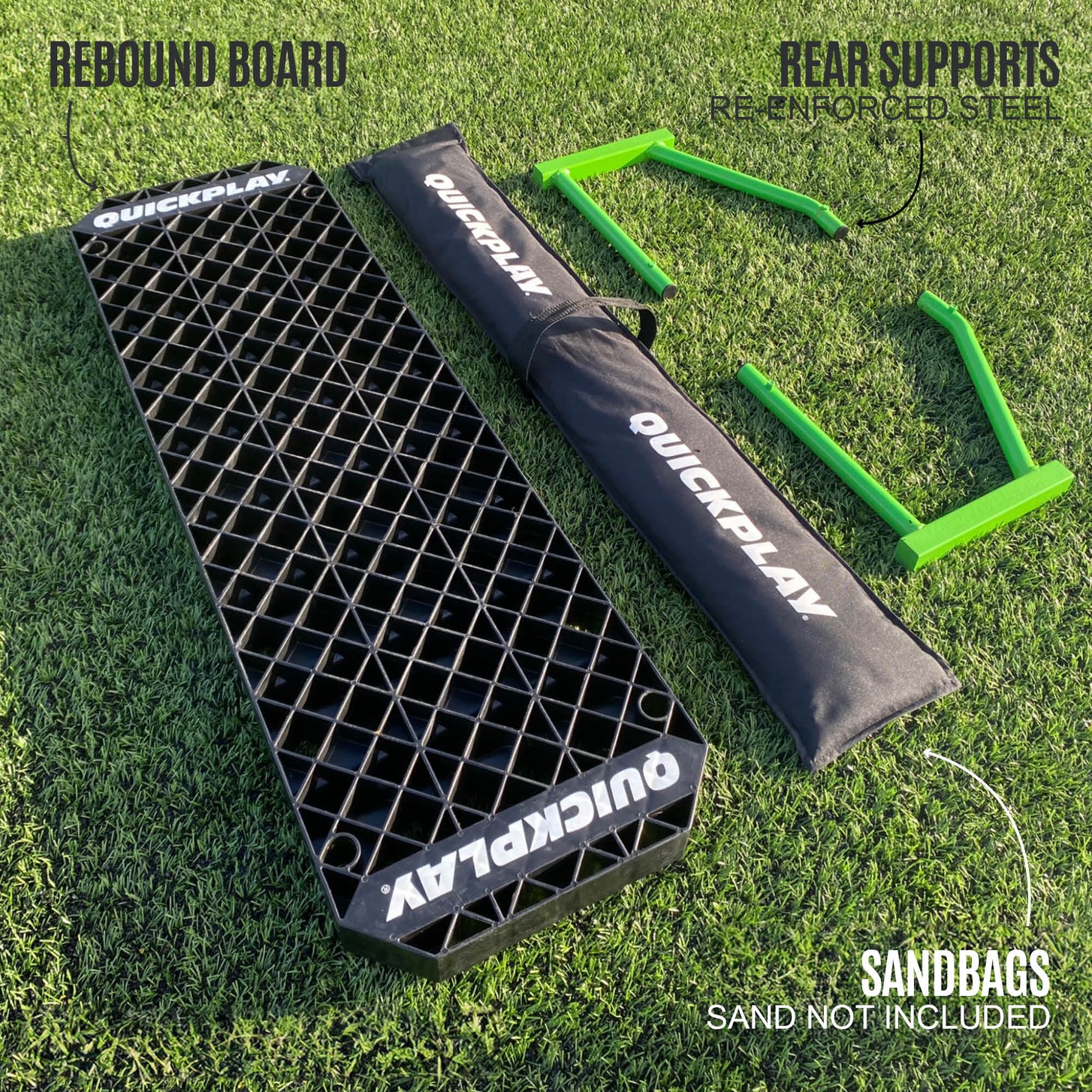 REPLAY Station XL parts laid out on grass: rebound board, black QUICKPLAY sandbag and two green rear supports, labeled "Sand not included".