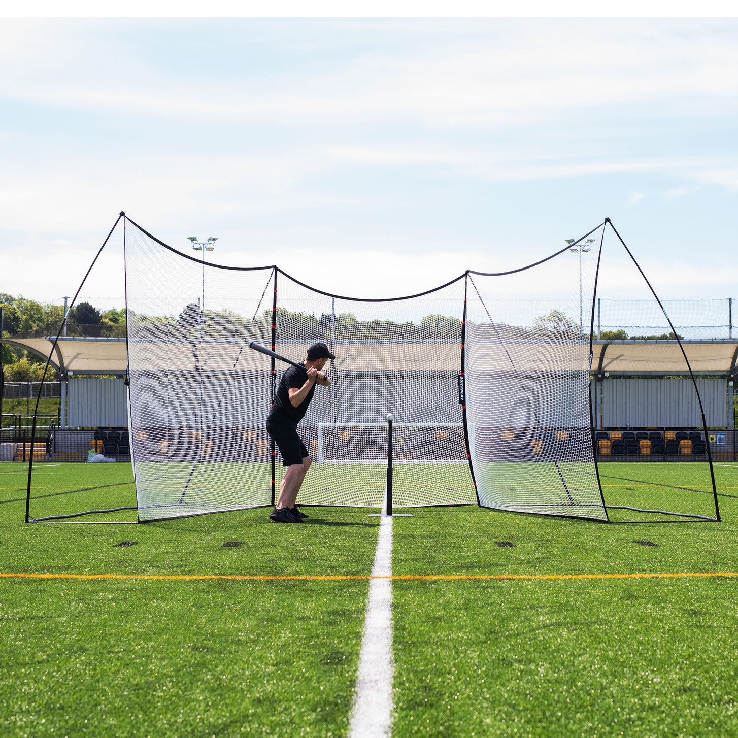 Batter ready to swing inside the U shape of the MEGA NET XL Multi Sport Backstop Net 32x9', seen from the front.