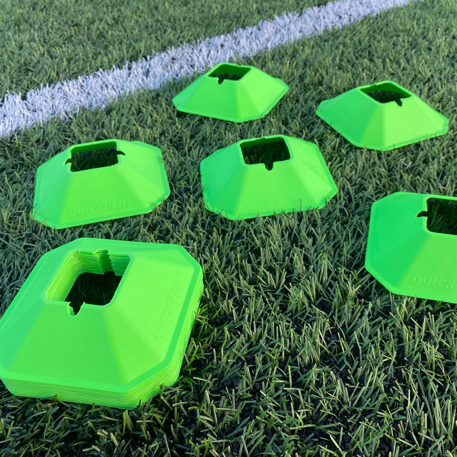 Green QUICKPLAY Mini Cones spread over artificial turf by a white line, with a stack of cones in front.