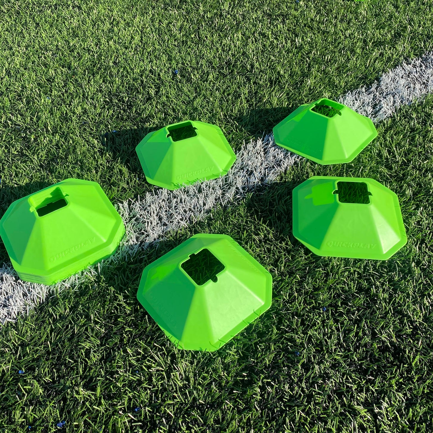 Five green QUICKPLAY Standard Cones laid out on artificial turf across a white field line.