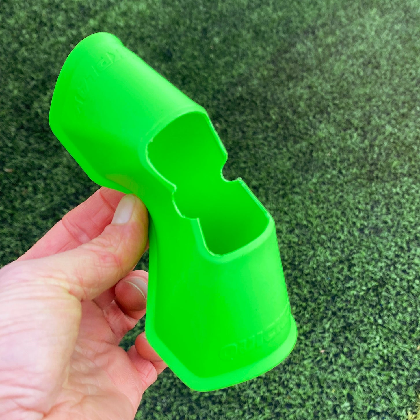 Hand folding a green QUICKPLAY Mini Cone over artificial turf to show how it bends.