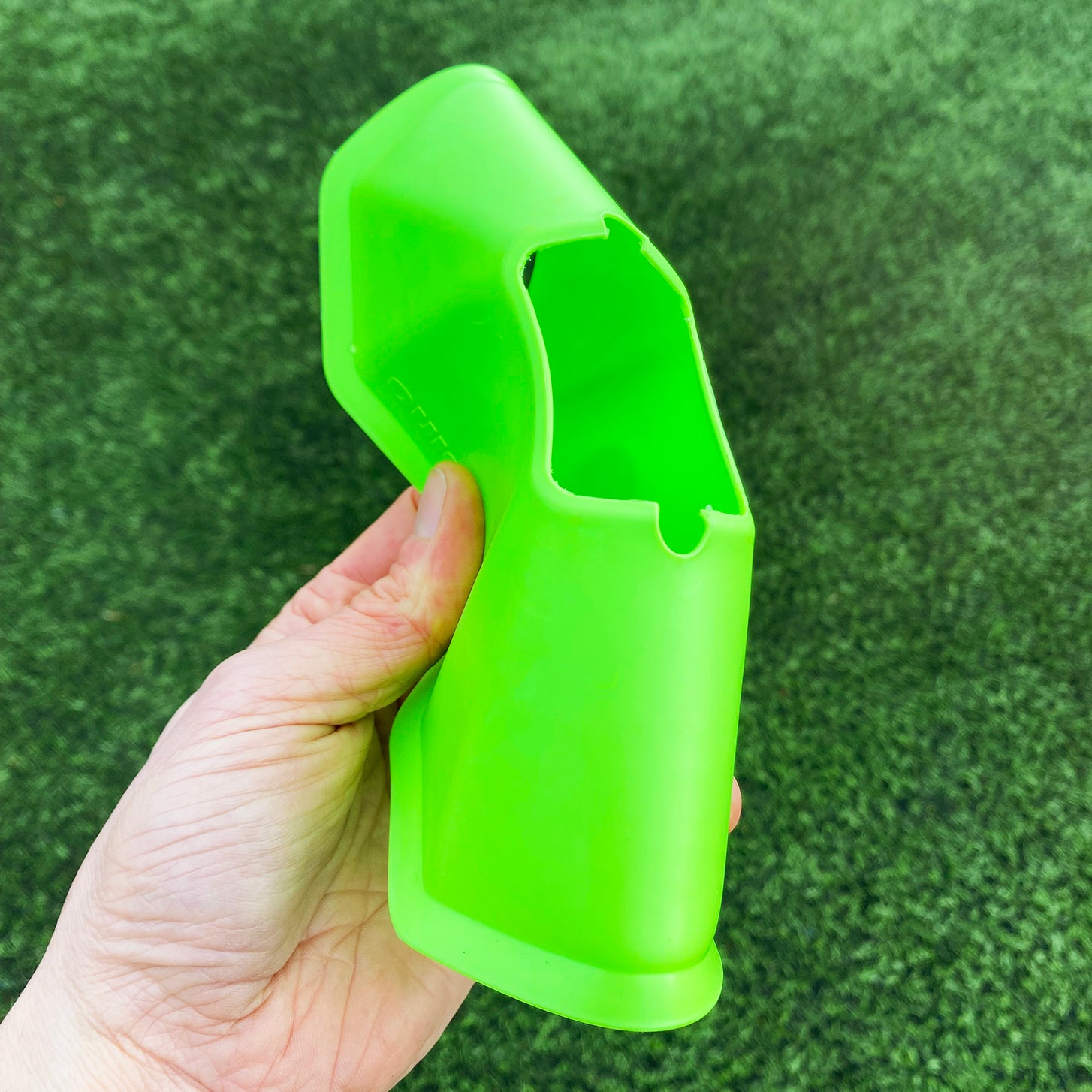 Hand bending a green QUICKPLAY Standard Cone in half over artificial turf to show the soft plastic.