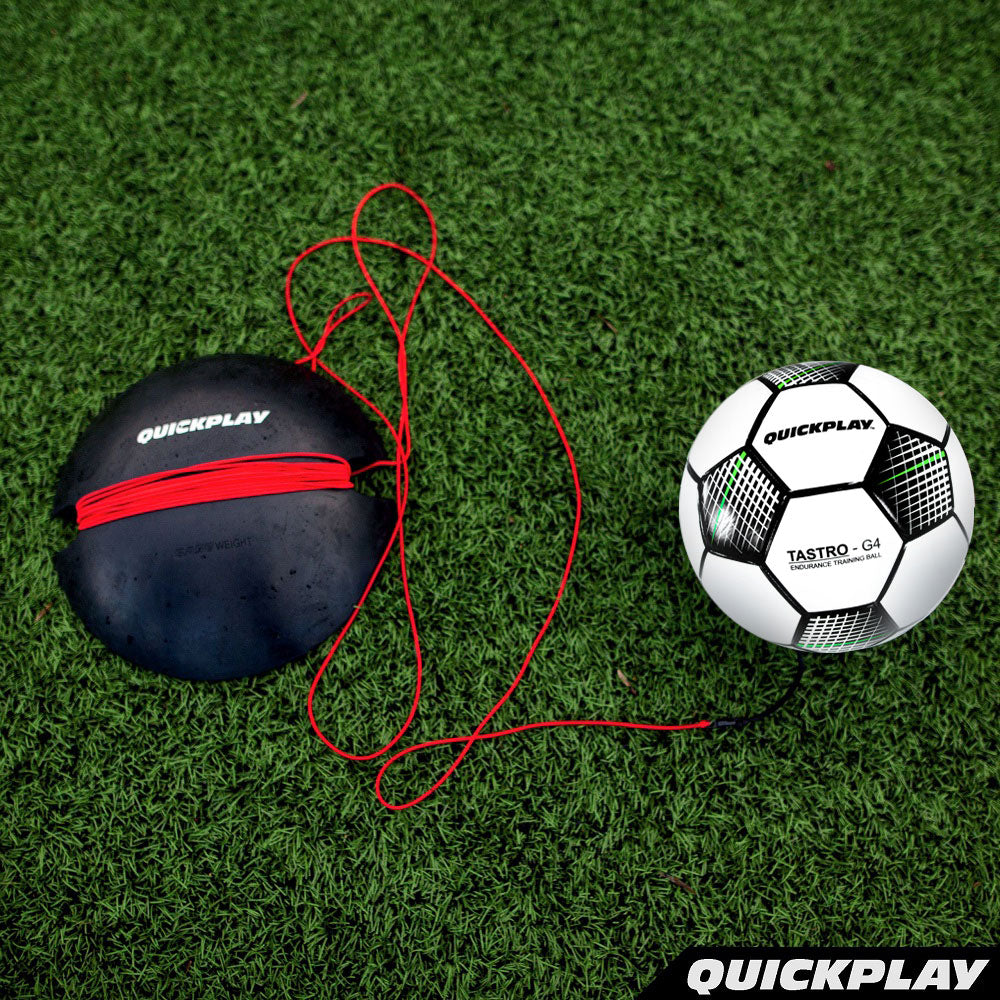 REPLAY Soccer Ball Trainer laid out on turf: black QUICKPLAY rubber base, red cord and white TASTRO ball, seen from above.