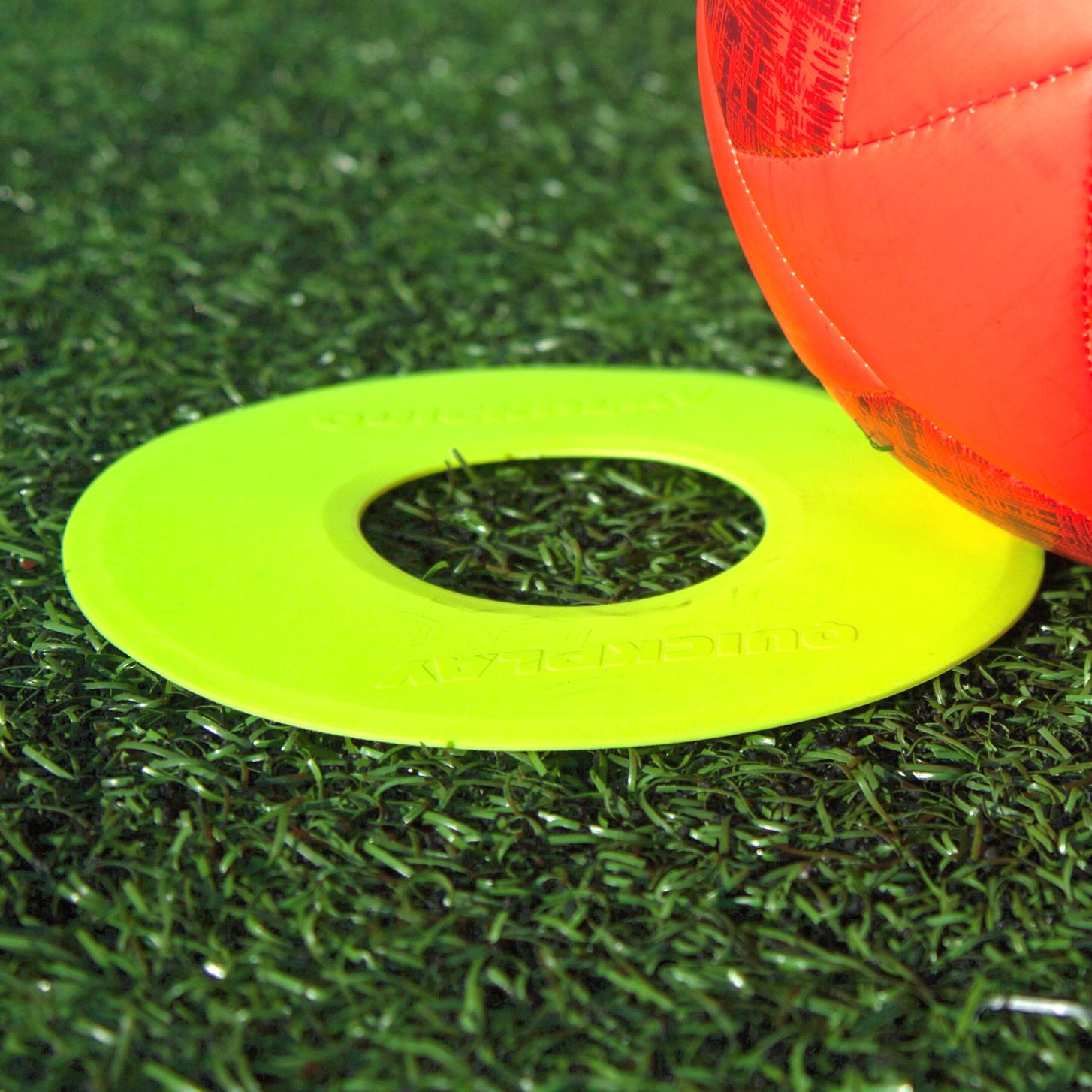 Neon yellow Flat Marker close up on artificial turf next to an orange soccer ball, with QUICKPLAY molded into it.